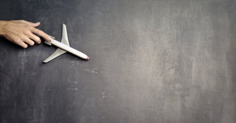 Global Shipping - Top view of crop anonymous person driving toy airplane on empty blackboard while representing journey concept