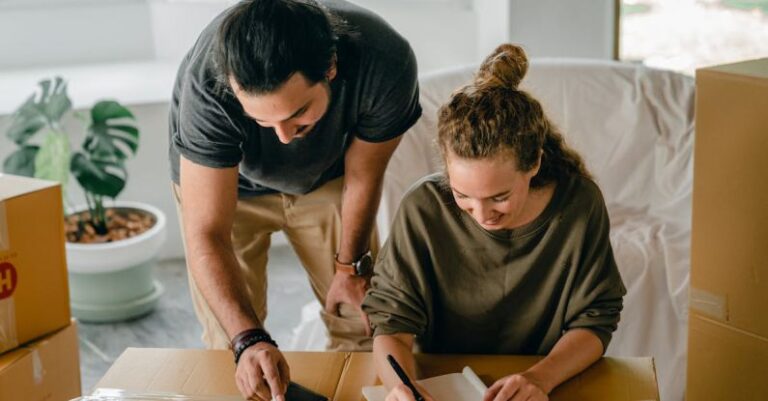 Real Estate Investment - Cheerful diverse couple writing in notebook near boxes before relocation