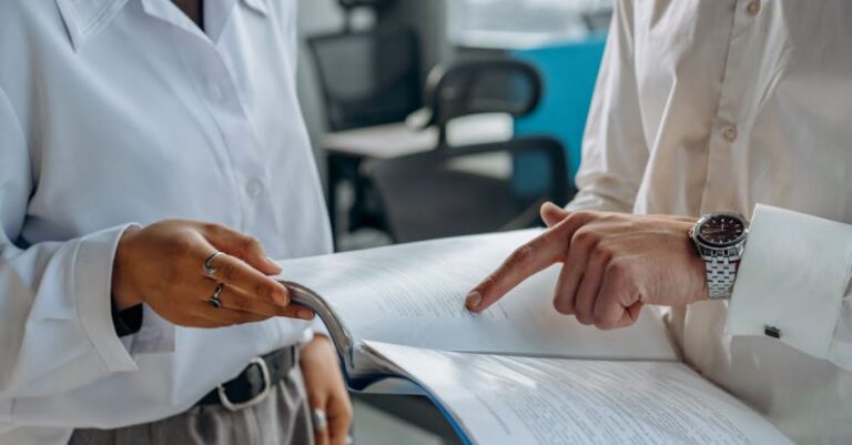 Financial Analysis Tools - Colleagues Standing in White Long Sleeve Shirts Discussing and Reading a Financial Report