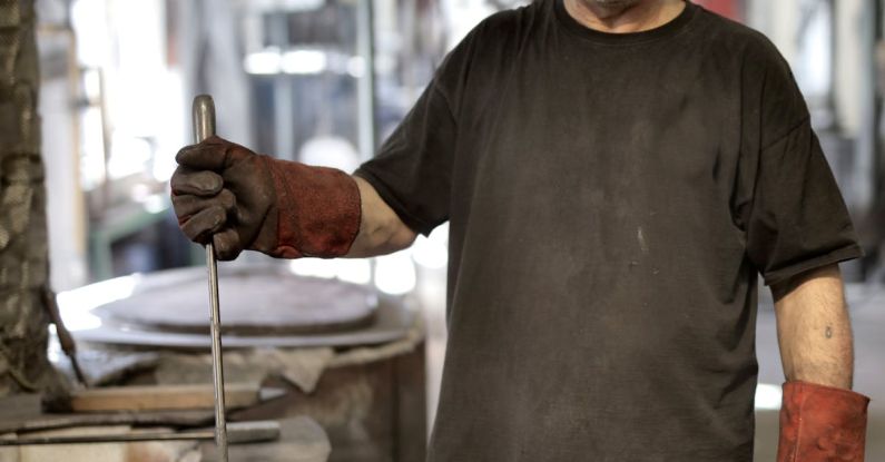 Additive Manufacturing - Elderly white hair craftsman in heavy duty gloves looking at camera while showing raw material in workshop