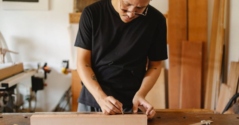 Smart Manufacturing - Crop serious ethnic male making marks on timber plank and working on wooden table in carpentry shop